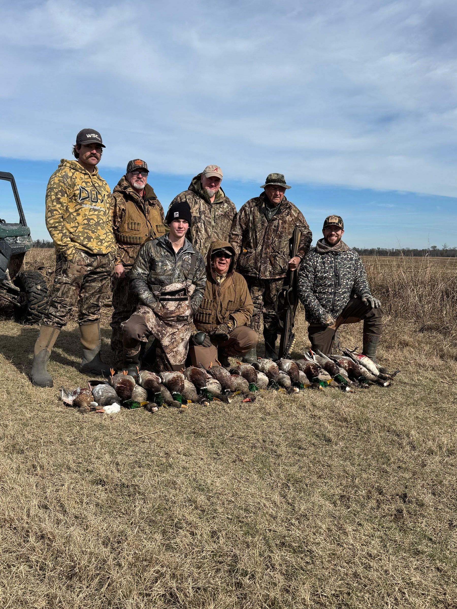 A Delta Outdoors hunting group kneeling behind ducks in a field after the hunt.