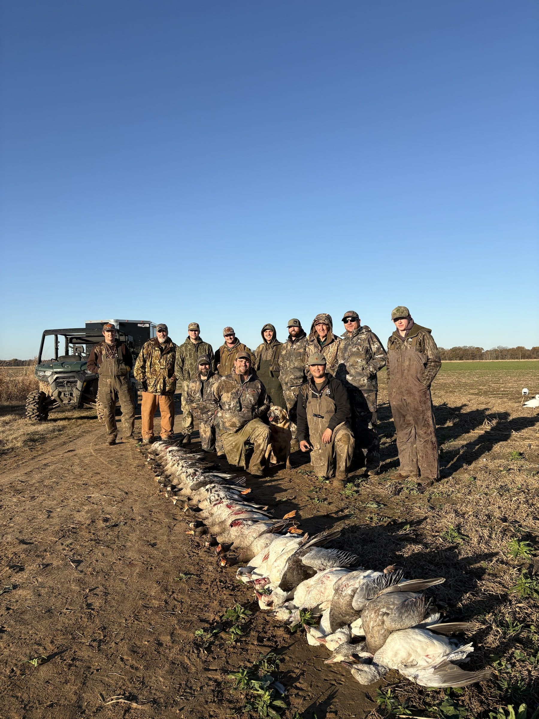 A large Delta Outdoors group posing in a field with birds lined out after a hunt.