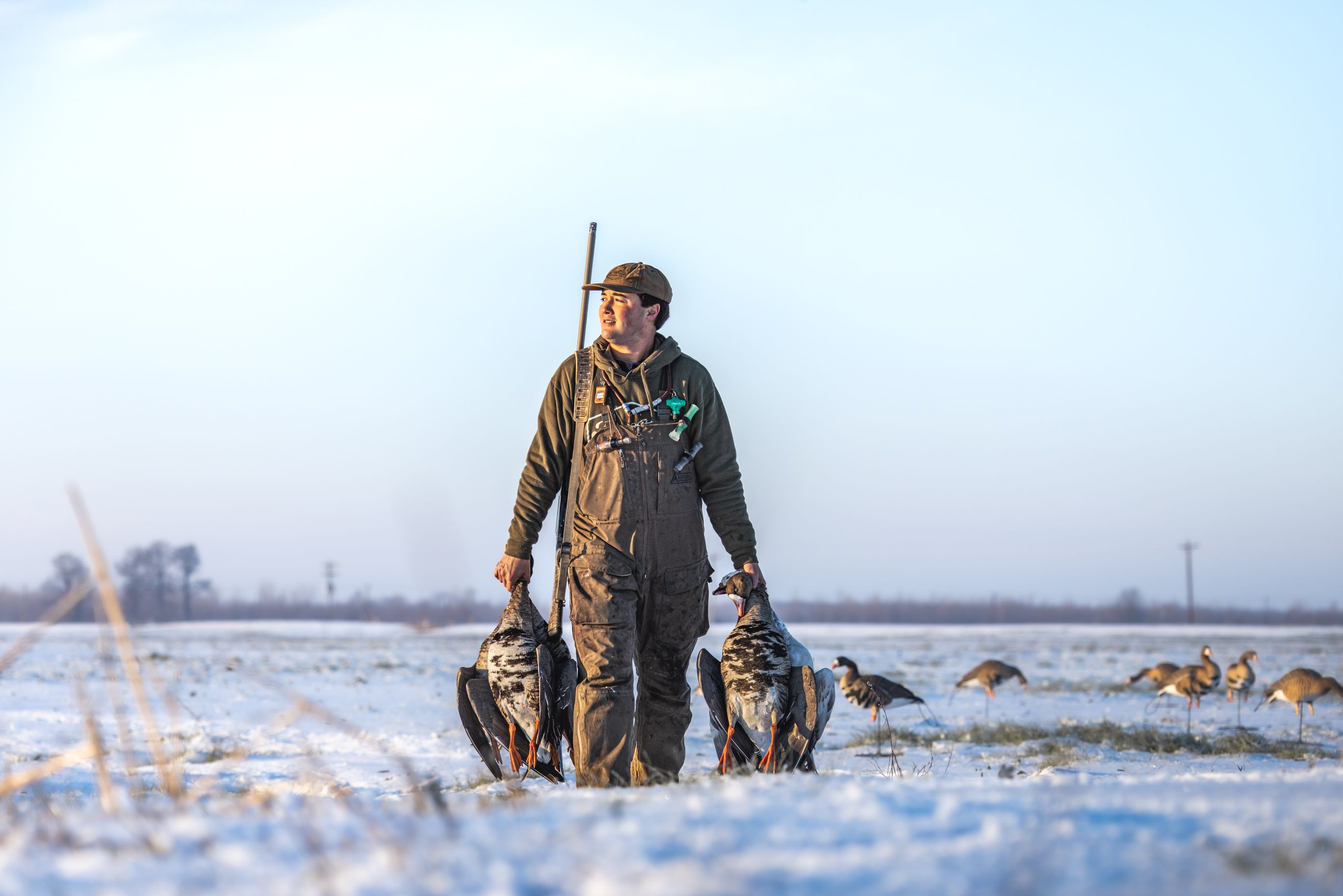 Waterfowl hunter carrying birds through a snowy decoy spread at Delta Outdoors Co.